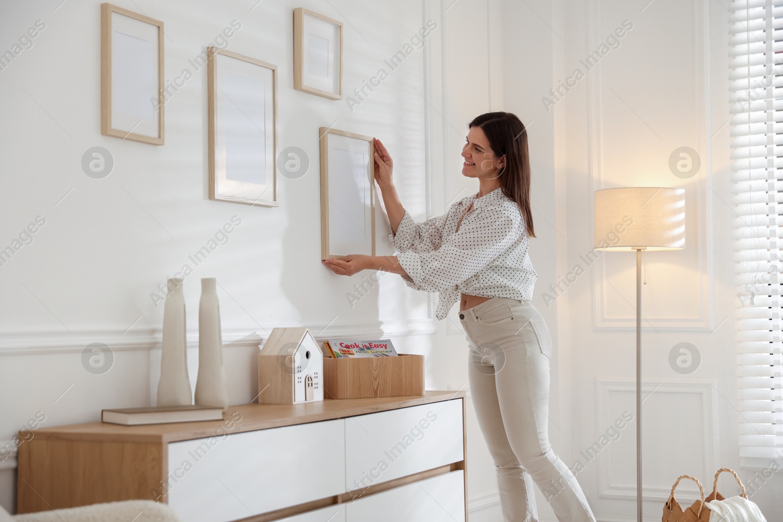Photo of Woman hanging blank frames on white wall indoors