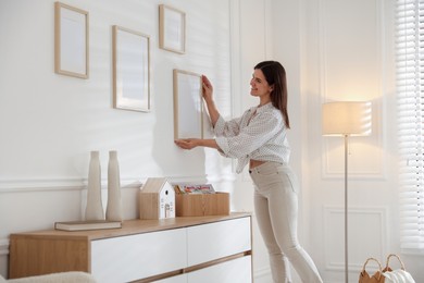 Photo of Woman hanging blank frames on white wall indoors
