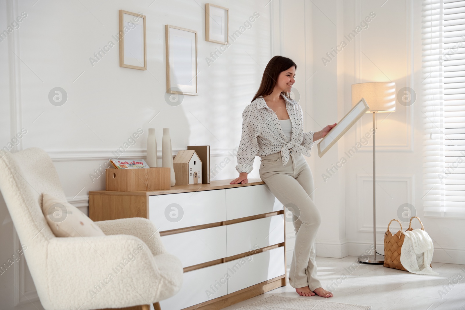 Photo of Woman hanging blank frames on white wall indoors