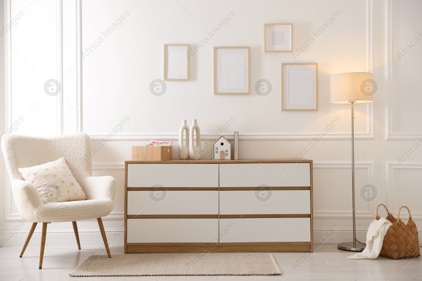 Photo of Blank frames on wall, armchair and chest of drawers indoors