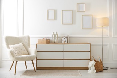 Photo of Blank frames on wall, armchair and chest of drawers indoors