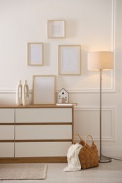Photo of Blank frames on wall and chest of drawers indoors