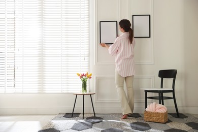 Photo of Woman hanging blank frames on white wall indoors, back view
