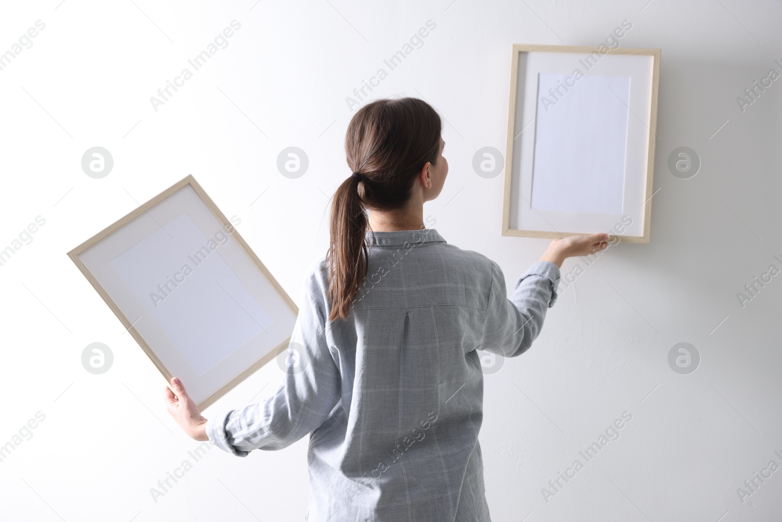 Photo of Woman hanging blank frames on white wall, back view