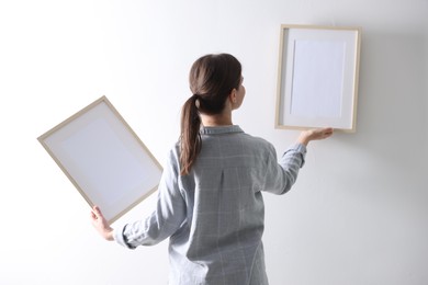 Photo of Woman hanging blank frames on white wall, back view