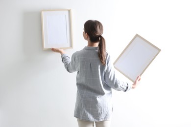 Photo of Woman hanging blank frames on white wall, back view