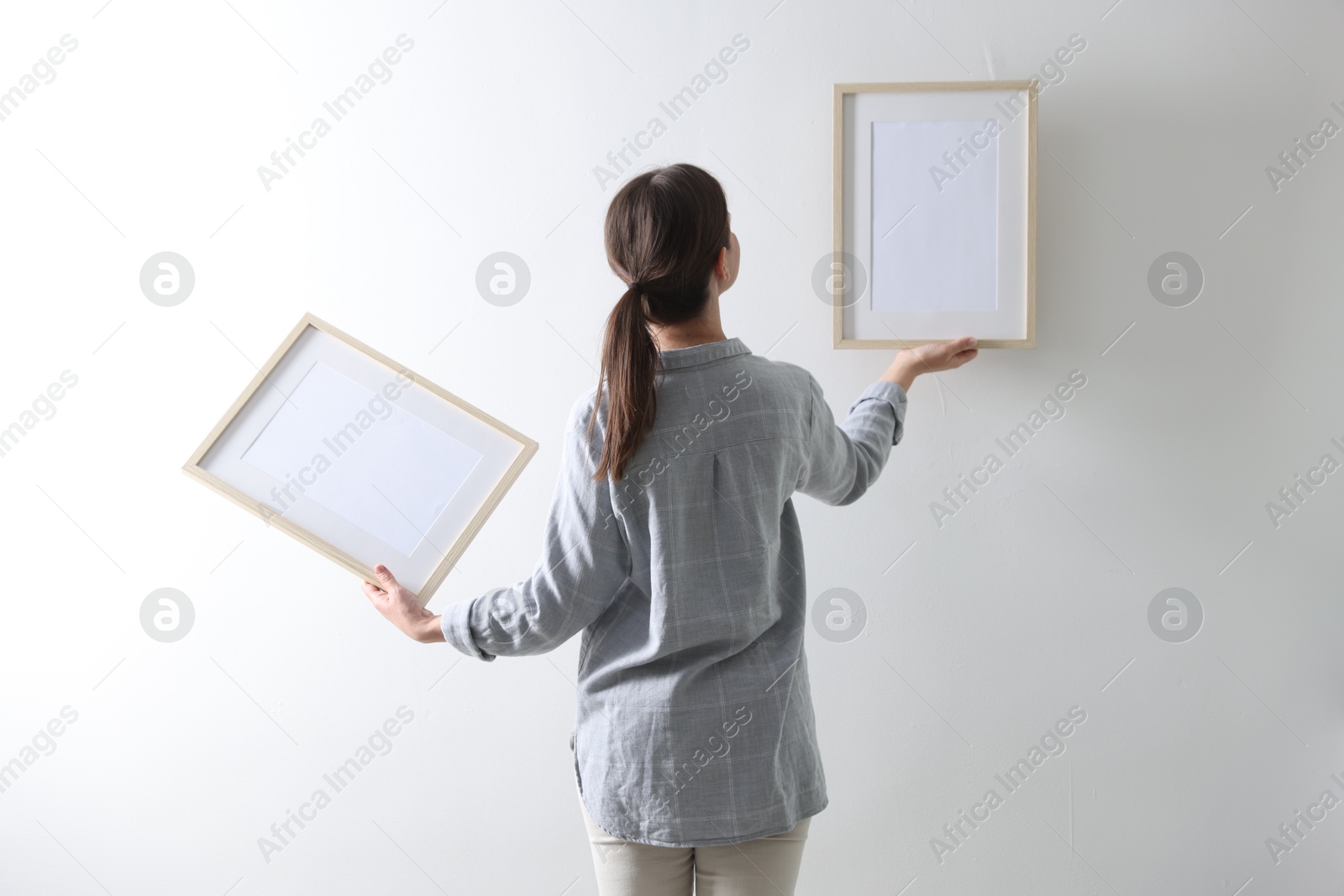 Woman hanging blank frames on white wall, back view Photo of Woman hanging blank frames on white wall, back view