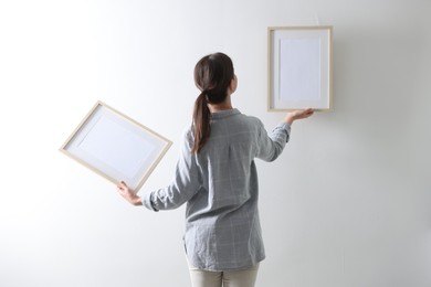 Photo of Woman hanging blank frames on white wall, back view