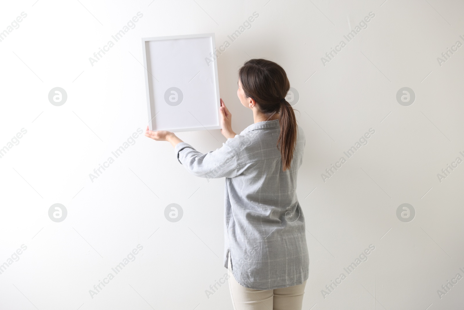 Woman hanging blank frame on white wall, back view Photo of Woman hanging blank frame on white wall, back view