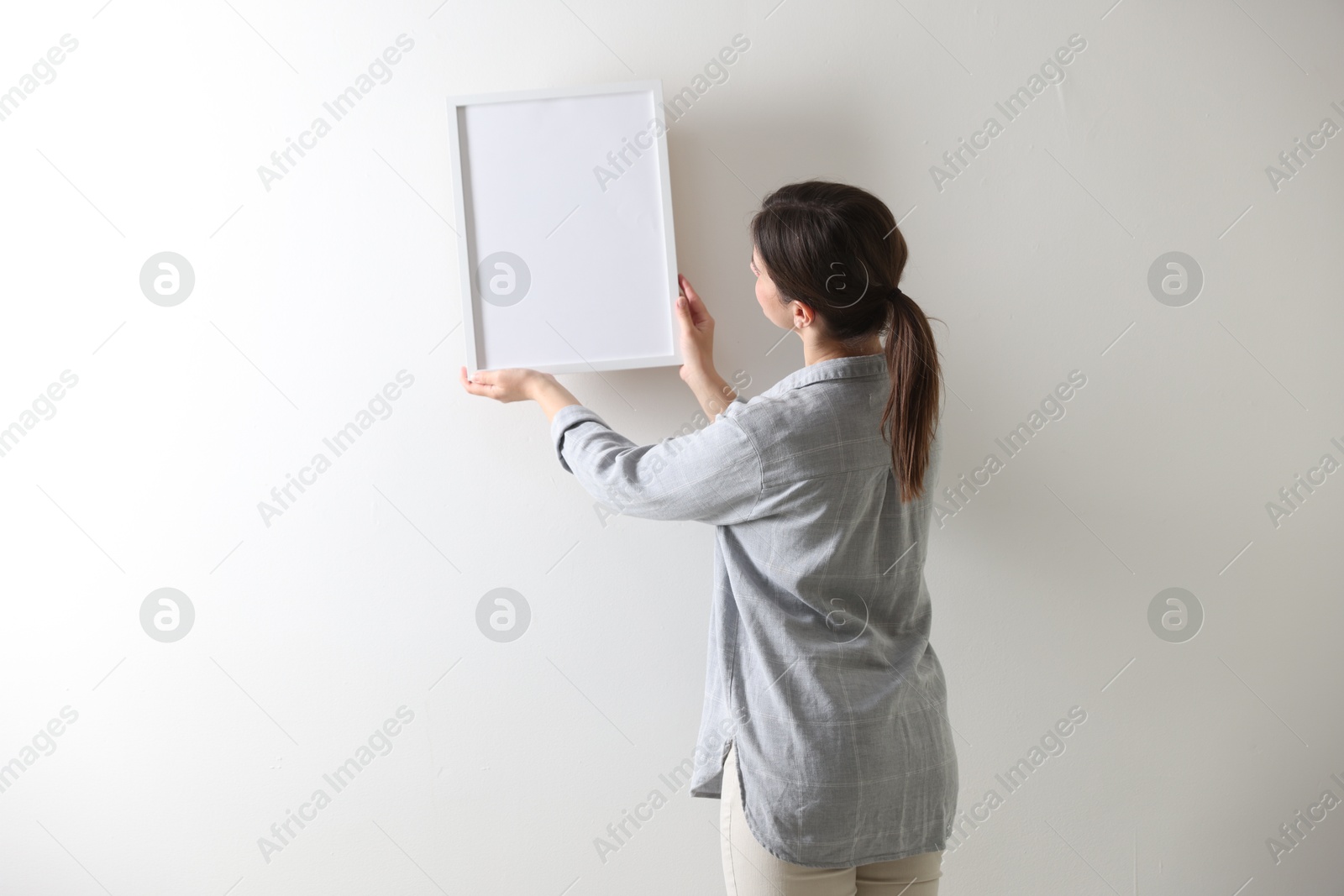 Woman hanging blank frame on white wall, back view Photo of Woman hanging blank frame on white wall, back view