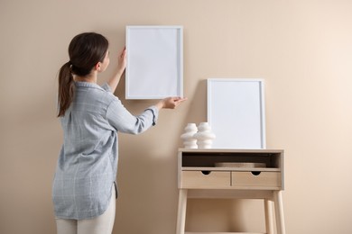 Photo of Woman hanging blank frame on beige wall, back view