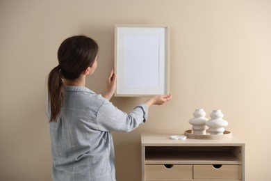 Photo of Woman hanging blank frame on beige wall, back view