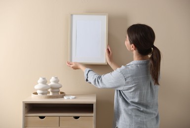 Photo of Woman hanging blank frame on beige wall, back view