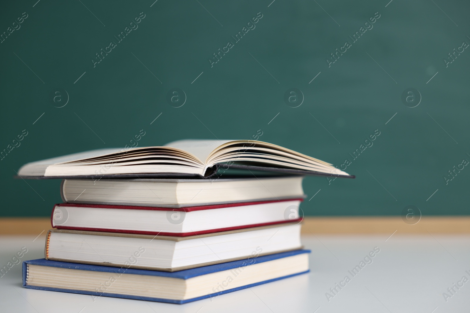 Stack of books on desk against chalkboard. Space for text Photo of Stack of books on desk against chalkboard. Space for text