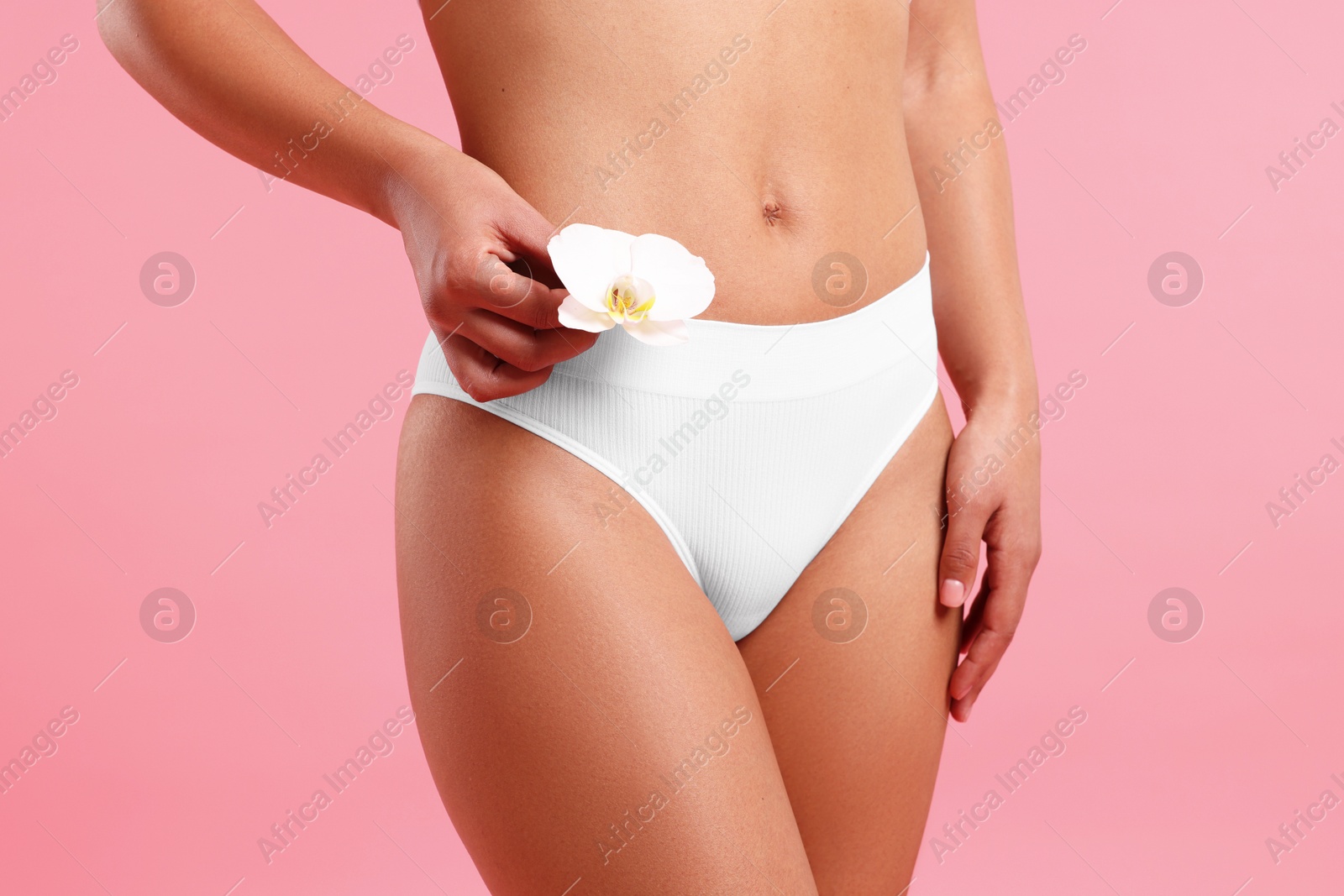 Photo of Woman in white underwear with flower showing smooth skin after epilation procedure on pink background, closeup