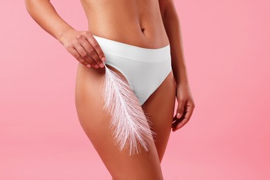 Photo of Woman in white underwear with feather showing smooth skin after epilation procedure on pink background, closeup