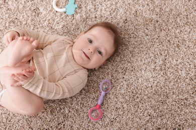 Photo of Cute little baby with rattle toy on floor at home, above view. Space for text
