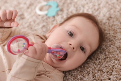 Photo of Cute little baby with rattle toy on floor at home