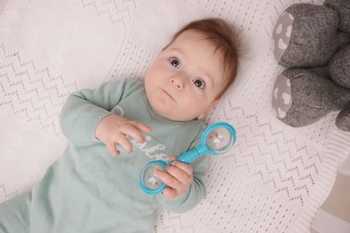 Photo of Cute little baby with rattle toy in crib at home, above view
