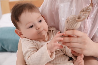 Photo of Mother and her cute little baby with rattle toy on bed at home, closeup
