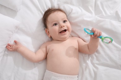 Photo of Cute little baby with rattle toy on bed at home, above view