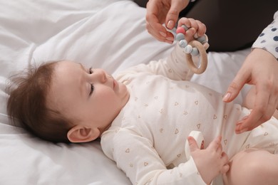 Photo of Mother and her cute little baby with rattle toy on bed at home, closeup