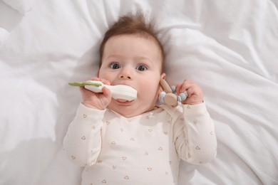 Photo of Cute little baby with rattle toy on bed at home, above view