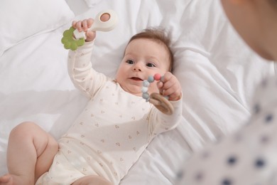 Photo of Mother and her cute little baby with rattle toy on bed at home, above view