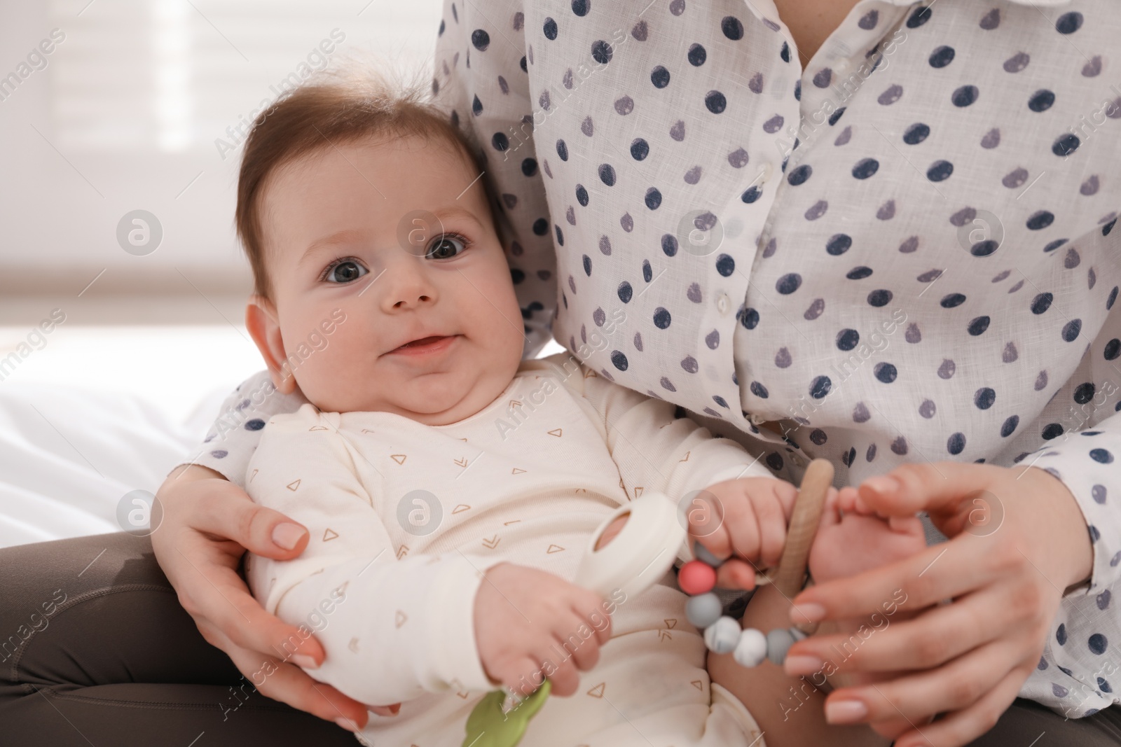 Mother and her cute little baby with rattle toy on bed at home, closeup Photo of Mother and her cute little baby with rattle toy on bed at home, closeup