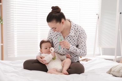 Photo of Mother and her cute little baby with rattle toy on bed at home