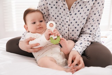 Photo of Mother and her cute little baby with rattle toy on bed at home, closeup