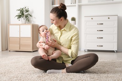 Photo of Mother and her cute little baby with rattle toy on floor at home