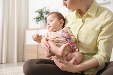 Photo of Mother and her cute little baby with rattle toy on floor at home, closeup