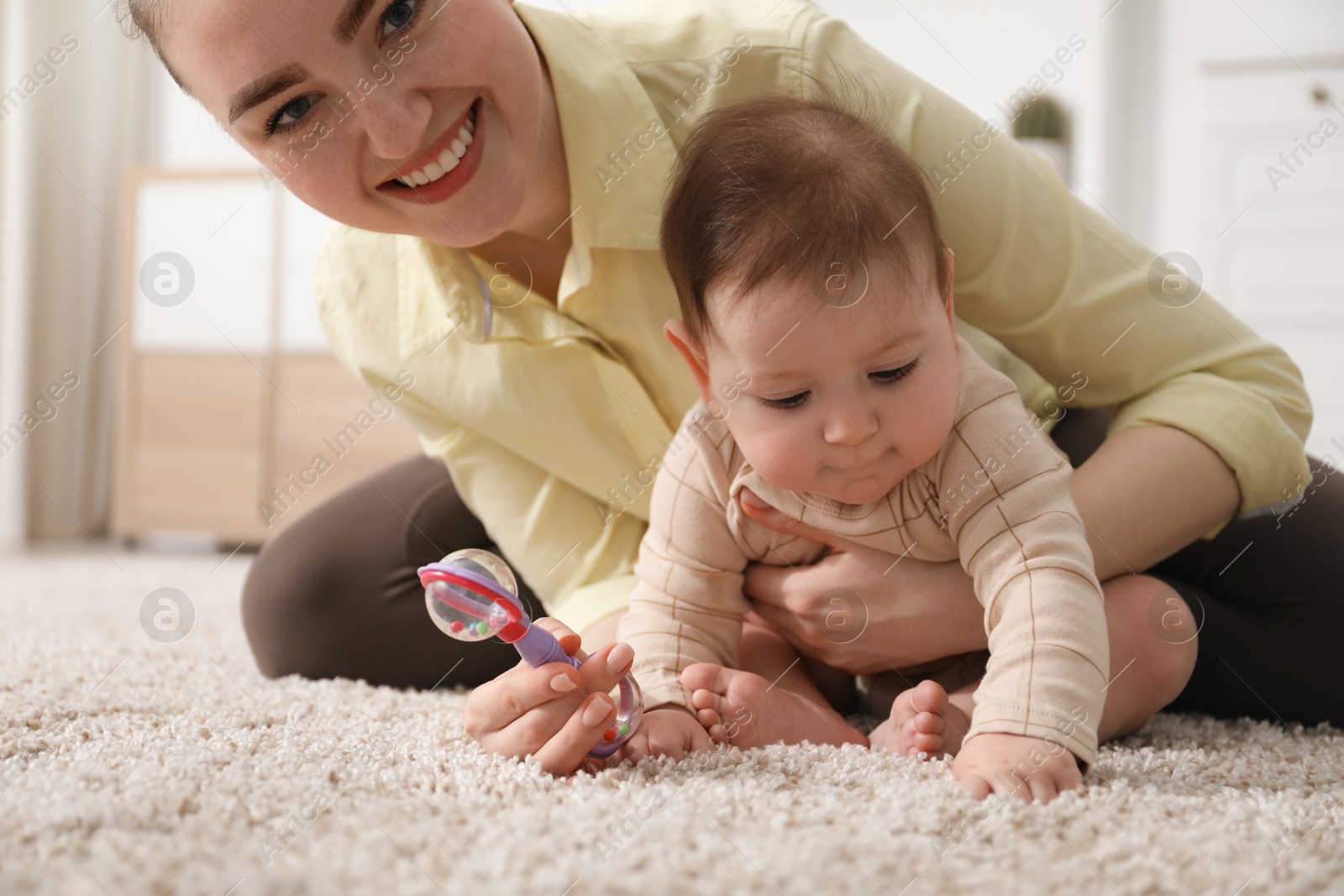 Mother and her cute little baby with rattle toy on floor at home Photo of Mother and her cute little baby with rattle toy on floor at home