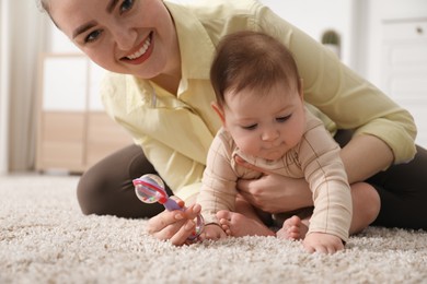 Photo of Mother and her cute little baby with rattle toy on floor at home