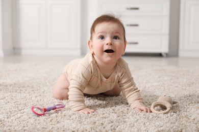 Photo of Cute little baby with rattle toy on floor at home
