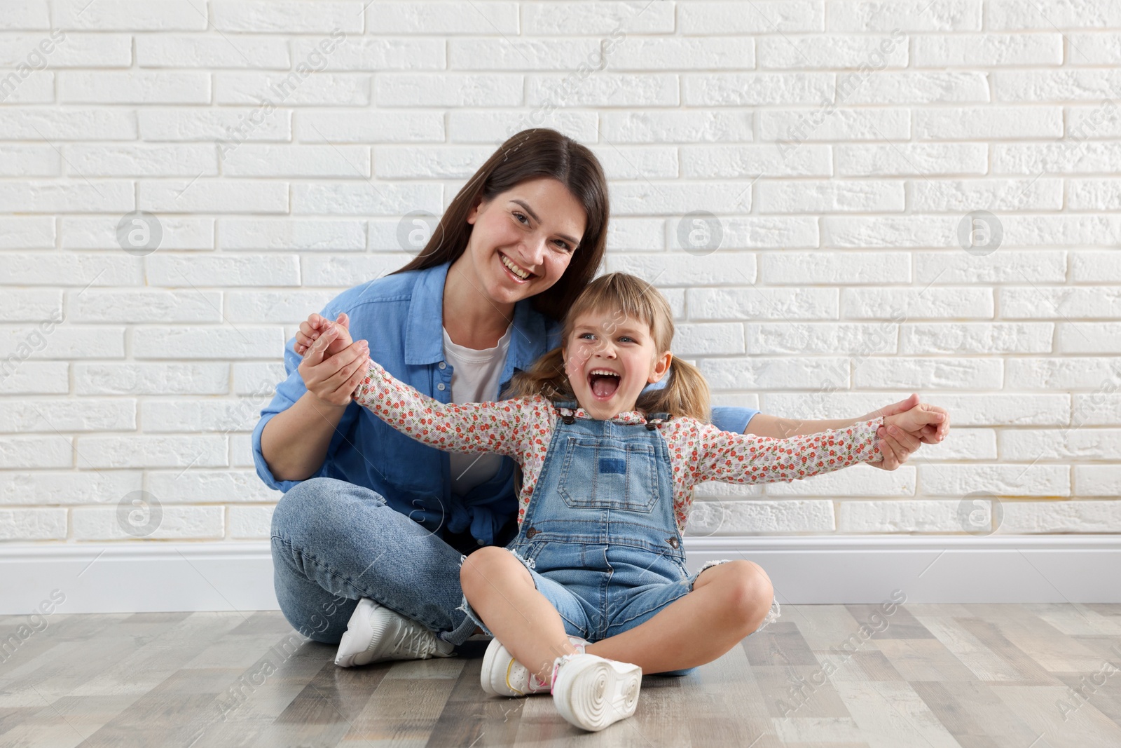 Beautiful mother and her little daughter near white brick wall Photo of Beautiful mother and her little daughter near white brick wall