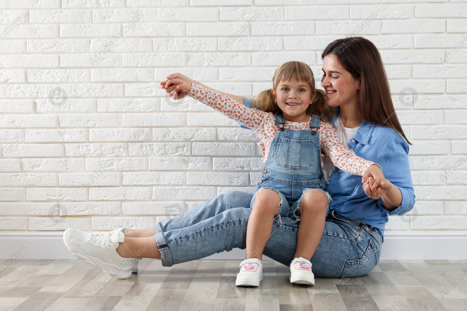 Beautiful mother and her little daughter near white brick wall. Space for text Photo of Beautiful mother and her little daughter near white brick wall. Space for text