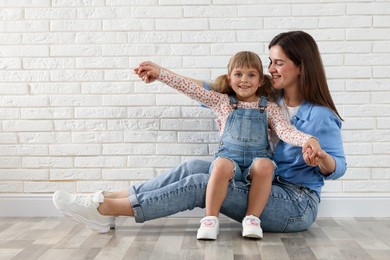 Photo of Beautiful mother and her little daughter near white brick wall. Space for text