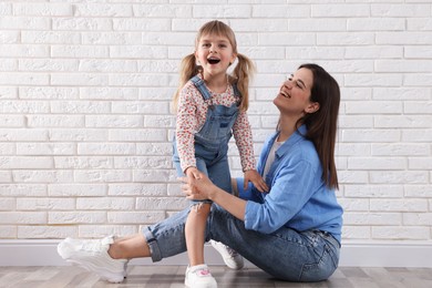 Photo of Beautiful mother and her little daughter near white brick wall