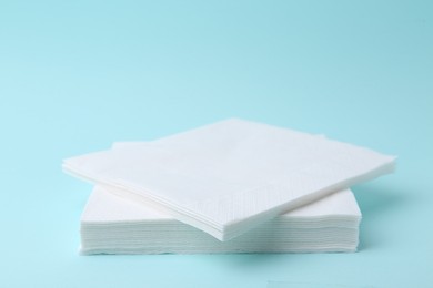 Photo of Stack of disposable paper handkerchiefs on light blue background, closeup. Space for text