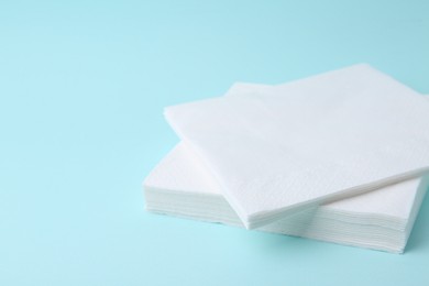 Photo of Stack of disposable paper handkerchiefs on light blue background, closeup. Space for text