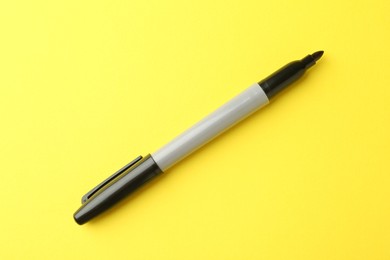 Photo of One black marker on yellow background, top view