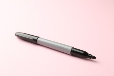 Photo of One black marker on light pink background, closeup. Space for text