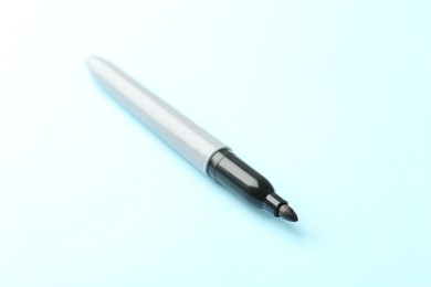 Photo of One black marker on light blue background, closeup. Space for text