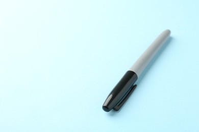 Photo of One black marker on light blue background, closeup. Space for text