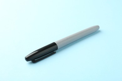 Photo of One black marker on light blue background, closeup. Space for text