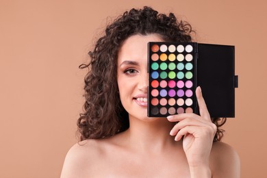 Photo of Smiling woman covering eye with eyeshadow palette on beige background