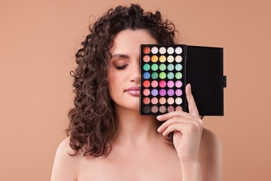 Photo of Woman covering eye with eyeshadow palette on beige background