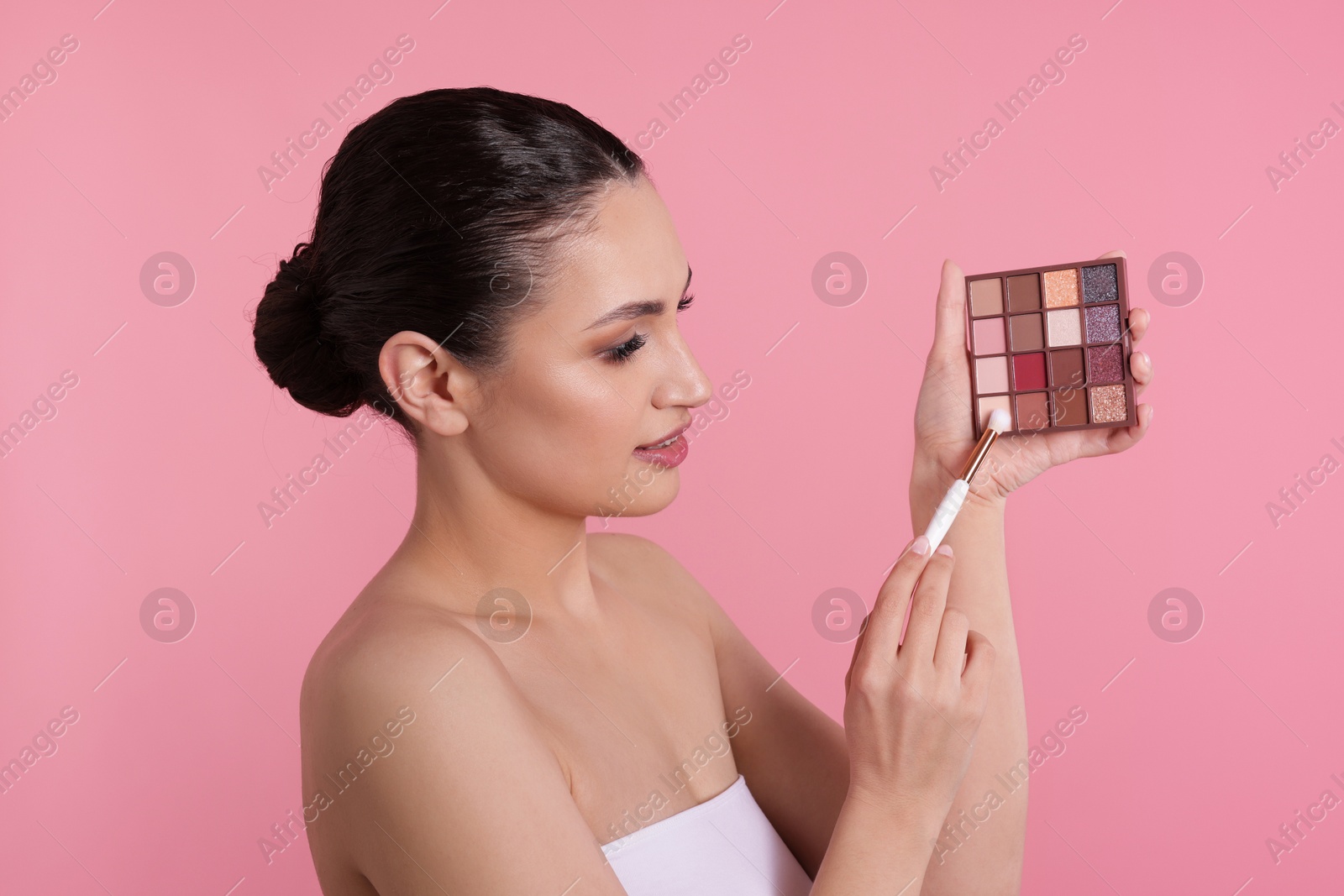 Woman with eyeshadow palette and brush on pink background Photo of Woman with eyeshadow palette and brush on pink background